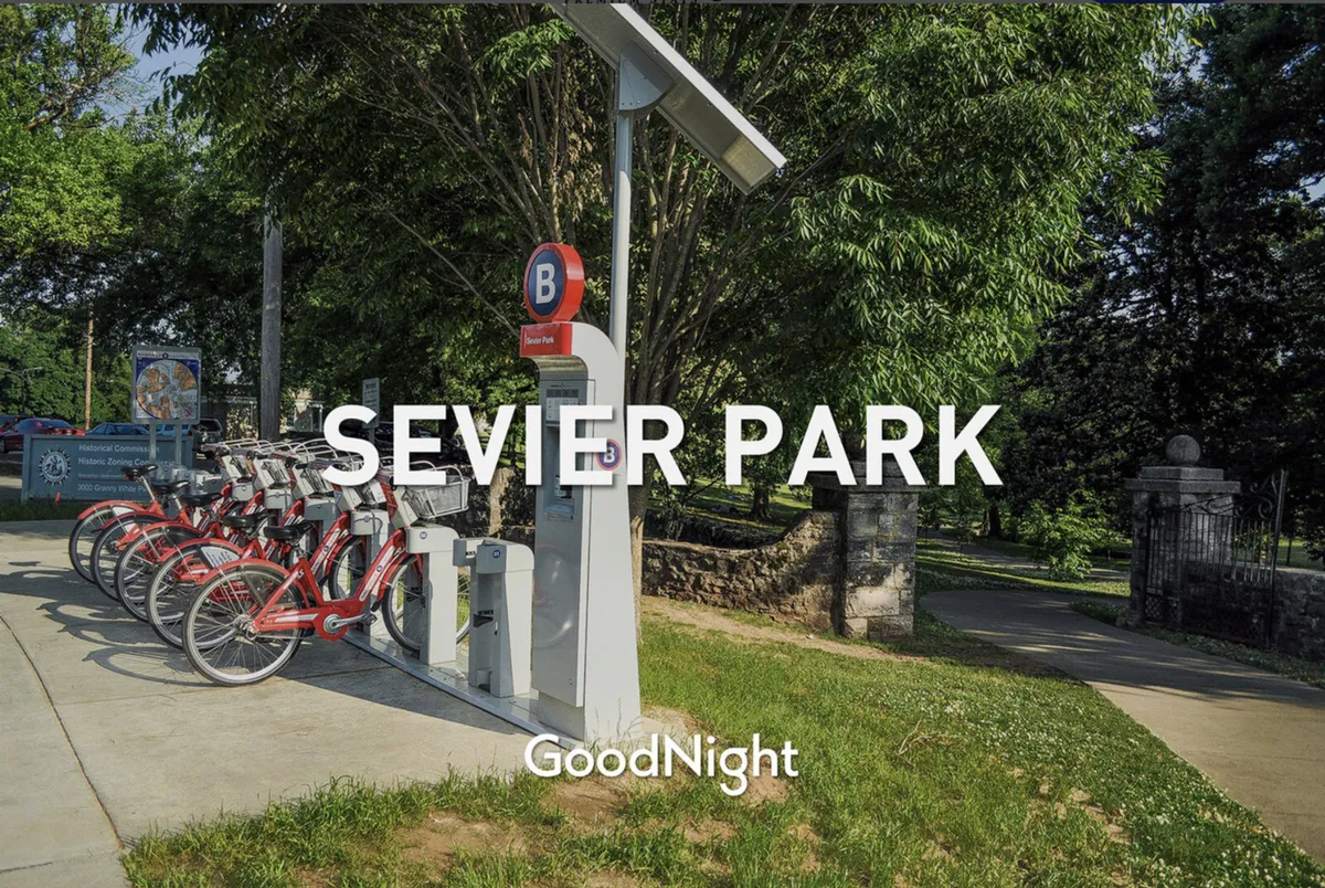 A bike rental station and park signage are visible, surrounded by greenery. The scene suggests an active, outdoor environment where visitors can bike, walk, or picnic, with a welcoming, social mood that resonates with family-friendly exploration of local parks.