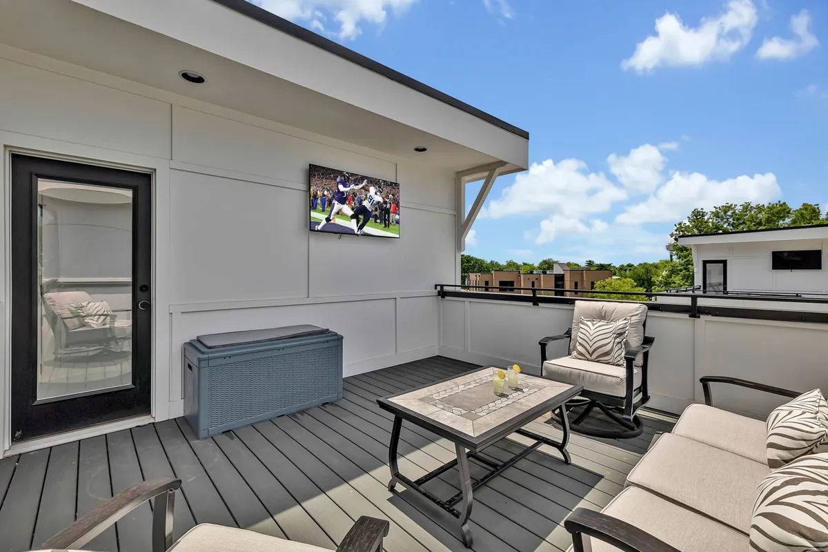 An inviting rooftop deck with an arrangement of outdoor sofas, a wall-mounted television, a central table decorated with candles, and a privacy wall. The ambiance is set for both relaxation and entertaining guests, with a view of the sky above.