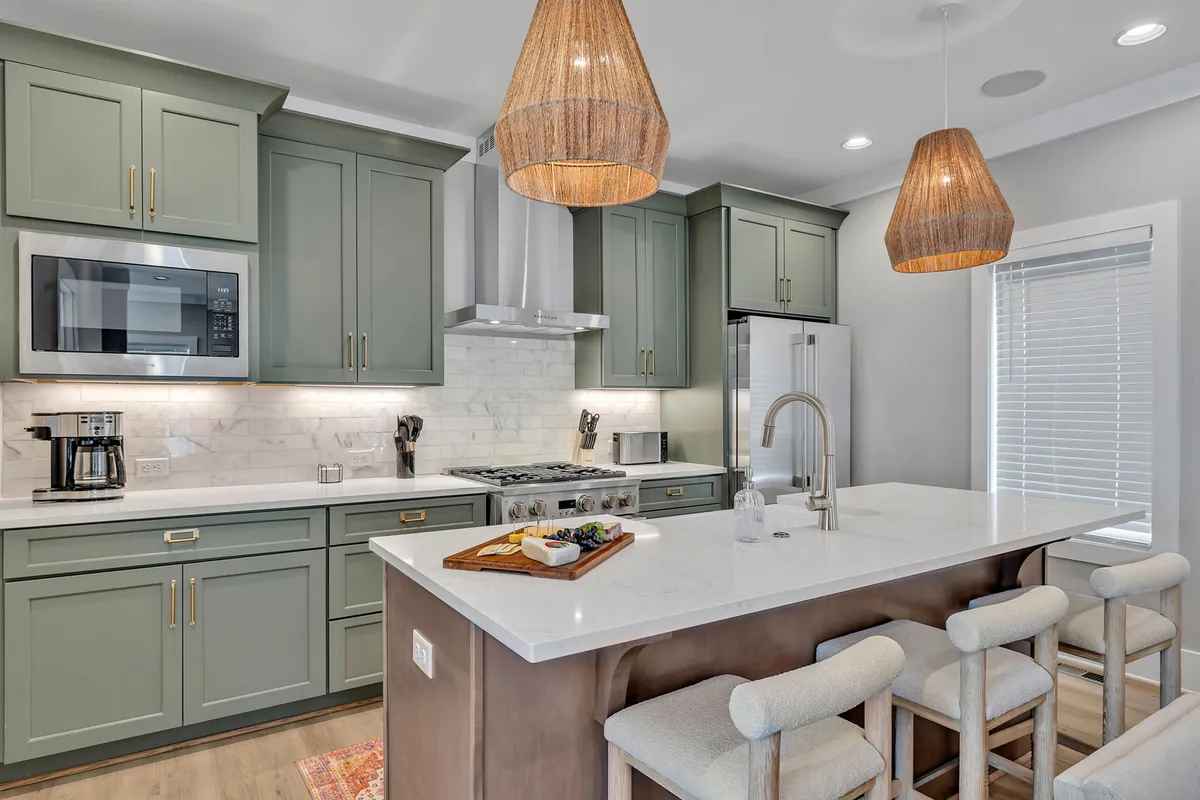 A warm, inviting kitchen scene showcasing a large island with bar seating, gleaming Monogram stainless-steel appliances, and stylish pendant lighting. The layout is ideal for collaborative cooking or casual breakfasts.